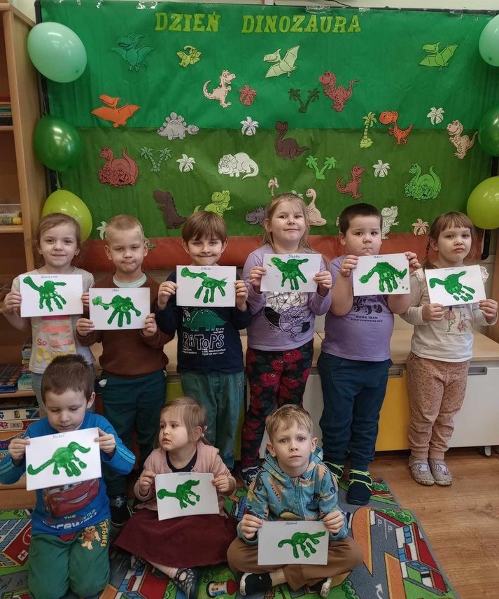 dzieci stoją, trzymają prace plastyczne - dzień dinozaura
